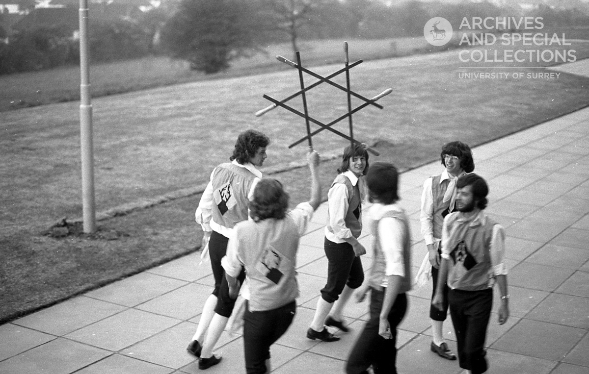 Photograph of Morris dancers. Their sticks are forming a star-shape, and a stag logo is visible on their outfits.