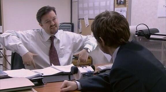 Film still of Ricky Gervais, sitting in the boss's chair, in his role in the TV show 'The Office'