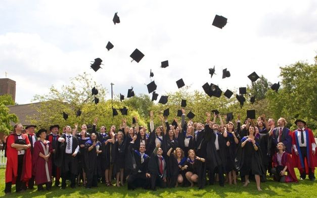 Student Graduating, crowds of students stood round in their graduation gowns throwing their hats in the air, professors wearing red either side   