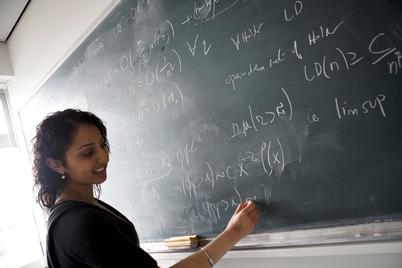 Maths student writing equations on a blackboard