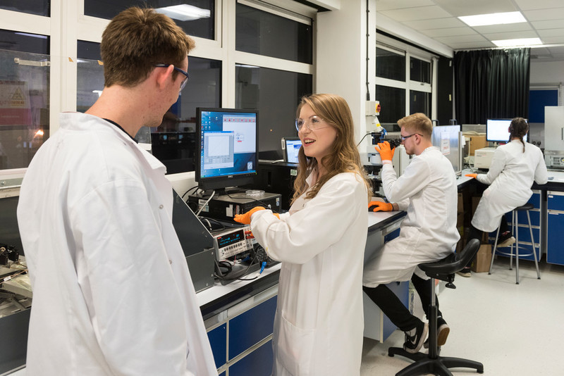 4 physics students wearing white coats and using equipment in a lab