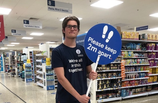 David in his part time role at Tesco's holding a 'Please keep 2m apart' sign