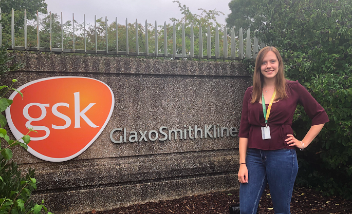 A picture of Chloe on her placement year, in front of a GSK sign at the GSK offices