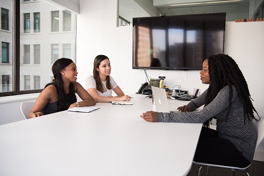 An interview candidate sitting opposite 2 interviewers. They are all seated at a large white table and all are smiling