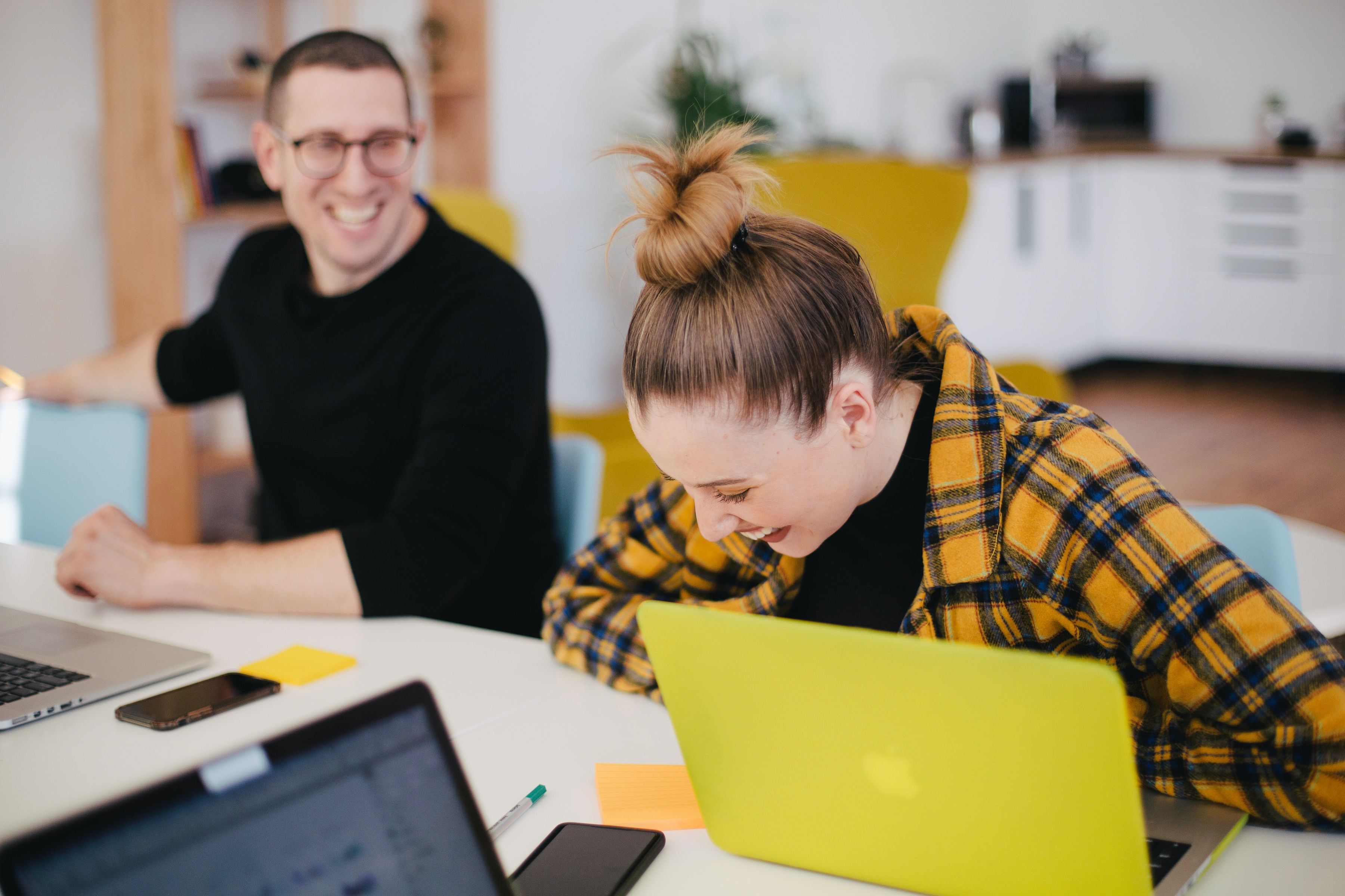 A male and female student laughing and working on laptops