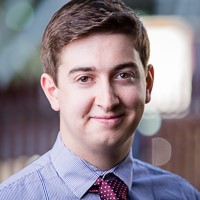 portrait photo of George Bowman from FDM. He is smiling and wearing a blue shirt and a tie.