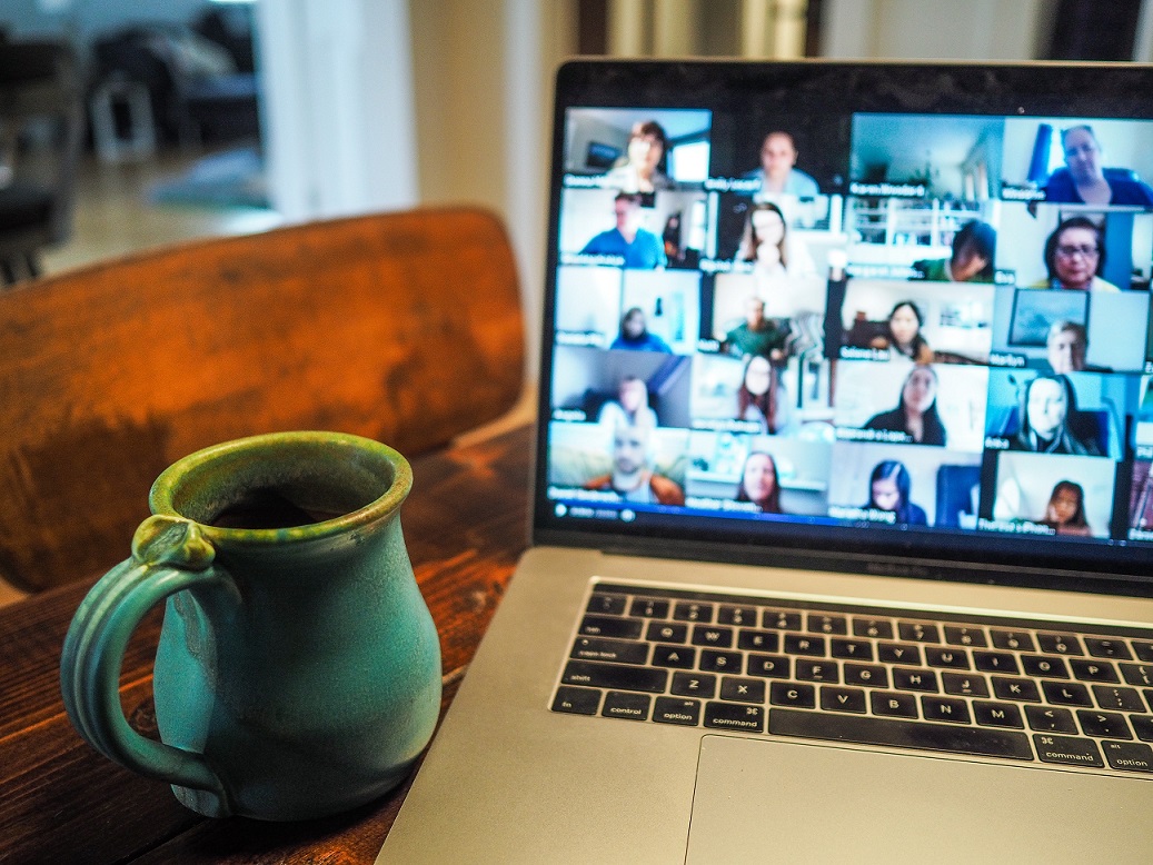 A laptop displaying a zoom chat with images of around 20 students on screen. A large mug is in the foreground