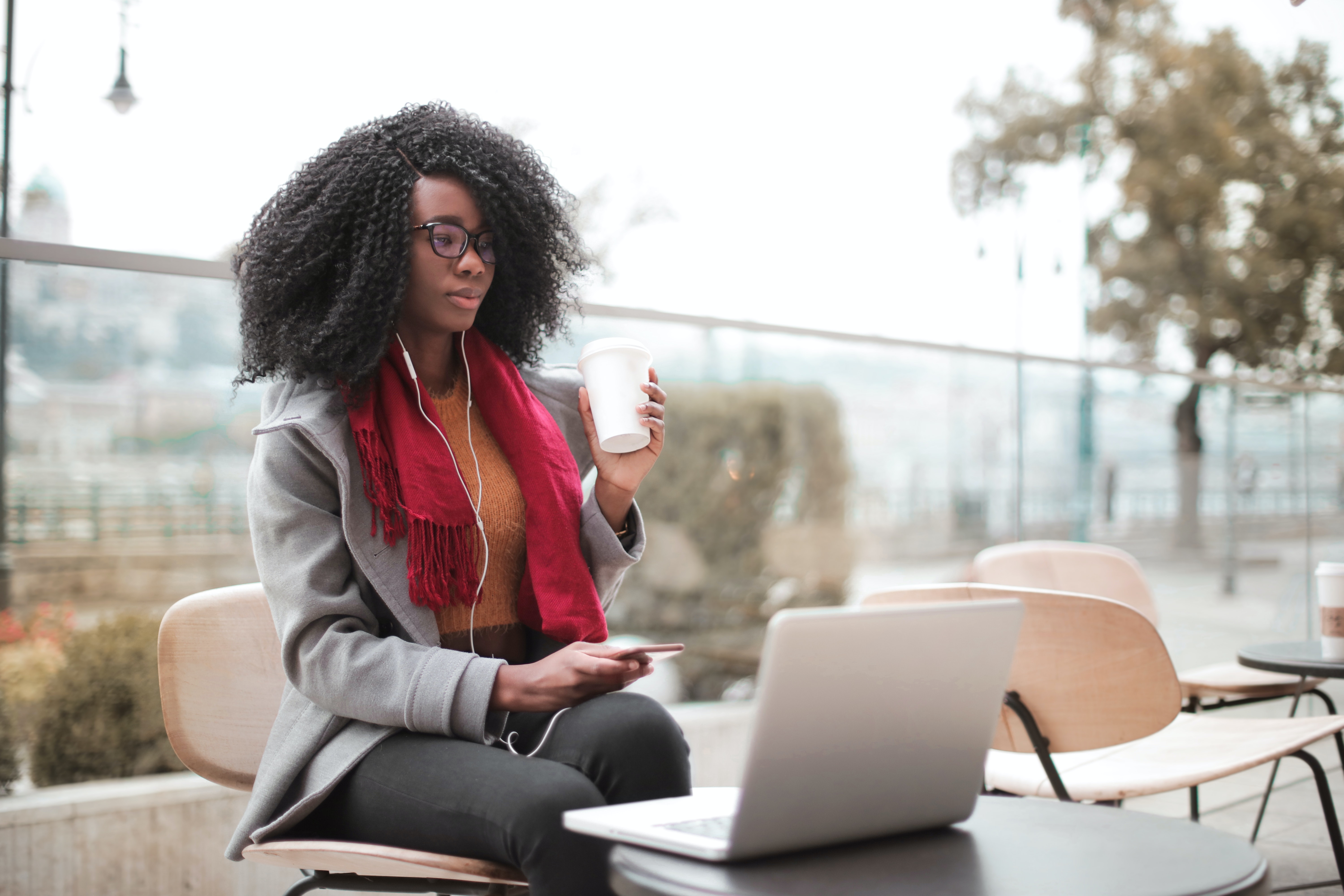 Lady with a laptop and mobile phone, wearing earphones and drinking from a disposable cup