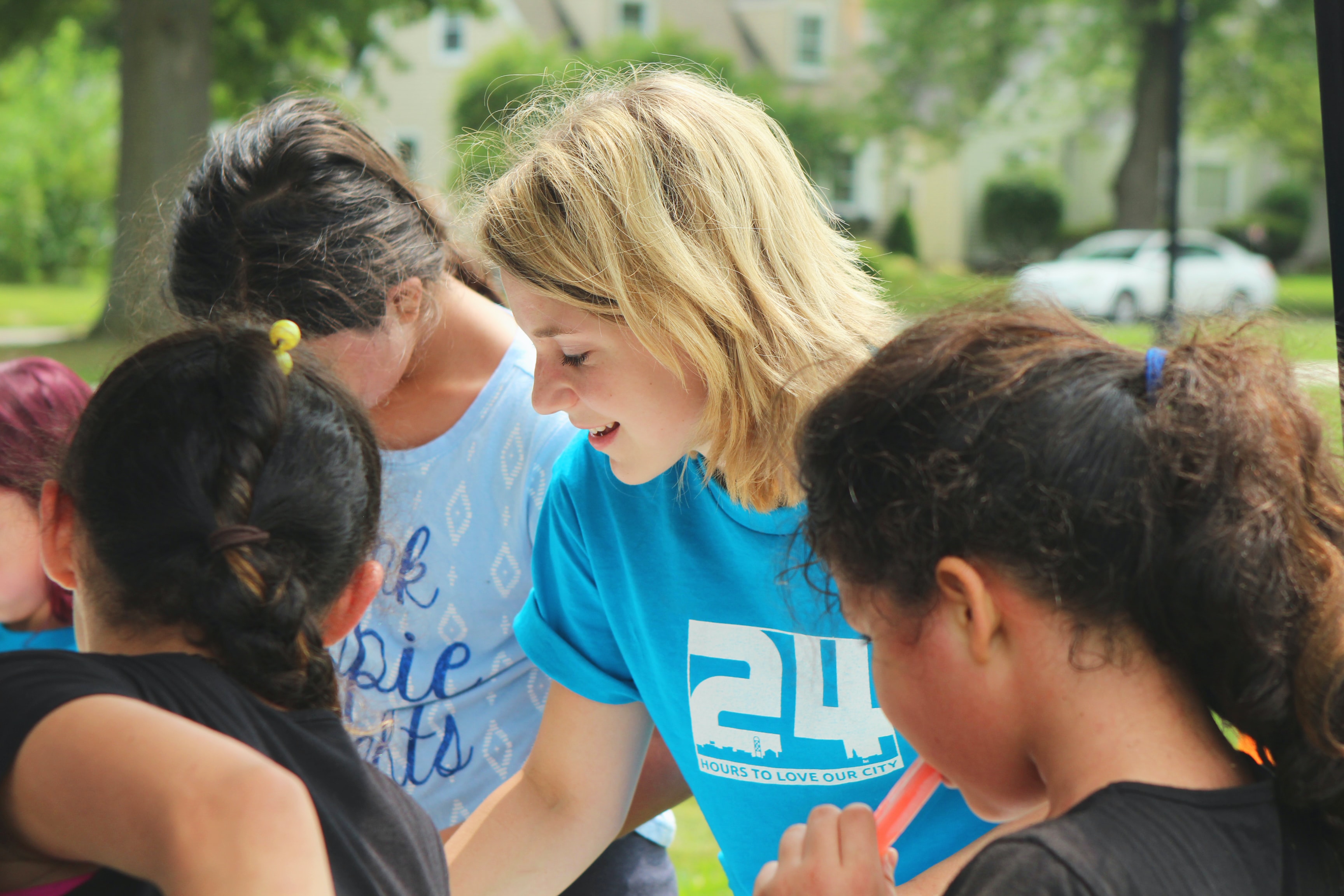 Young woman in a blue t-shirt with'24' on it. She is helping some children who are looking at something she is showing them.