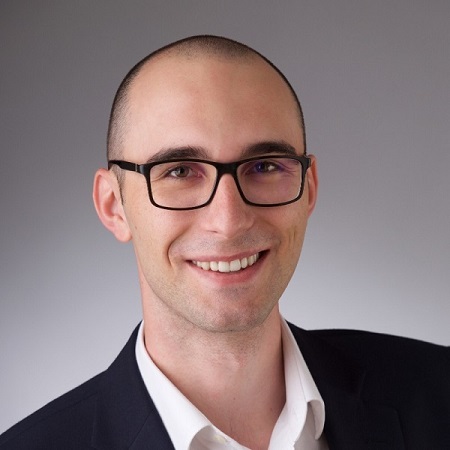 A headshot of Aron. He is wearing dark rimmed glasses and is smiling.