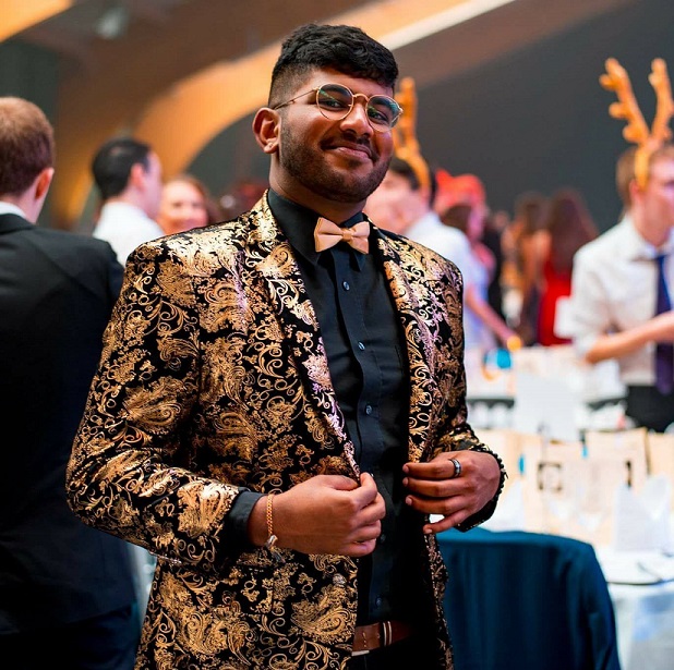 Gilan wearing a sparkly gold jacket and bow tie and black shirt. He is at a Christmas function.