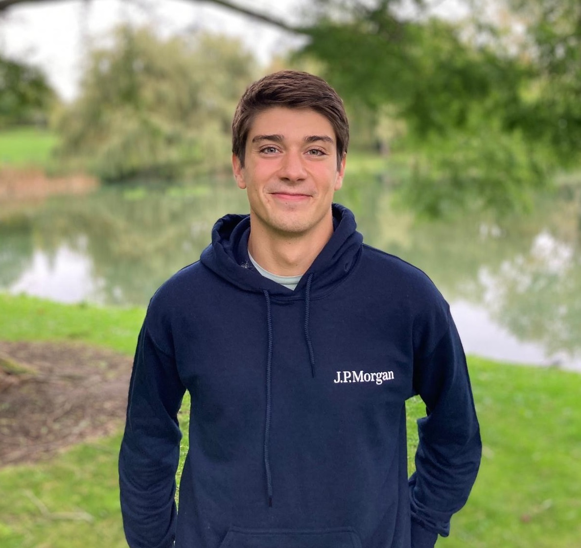 Joao wearing a JP Morgan hoodie, standing by the lake at University of Surrey