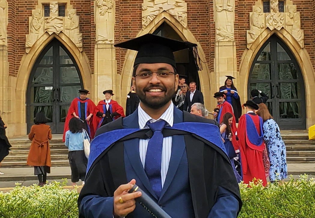 Harsha, wearing graduation cap and gown in front of Guildford Cathedral