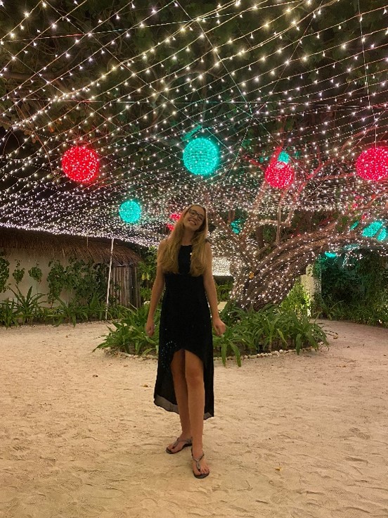 Victoria wearing a smart black dress standing below a ceiling of fairy lights