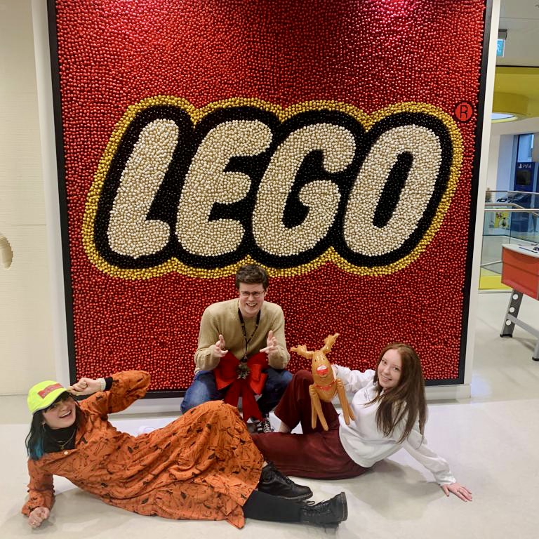 Nadia and her two fellow interns posing in front of a sparkly lego sign