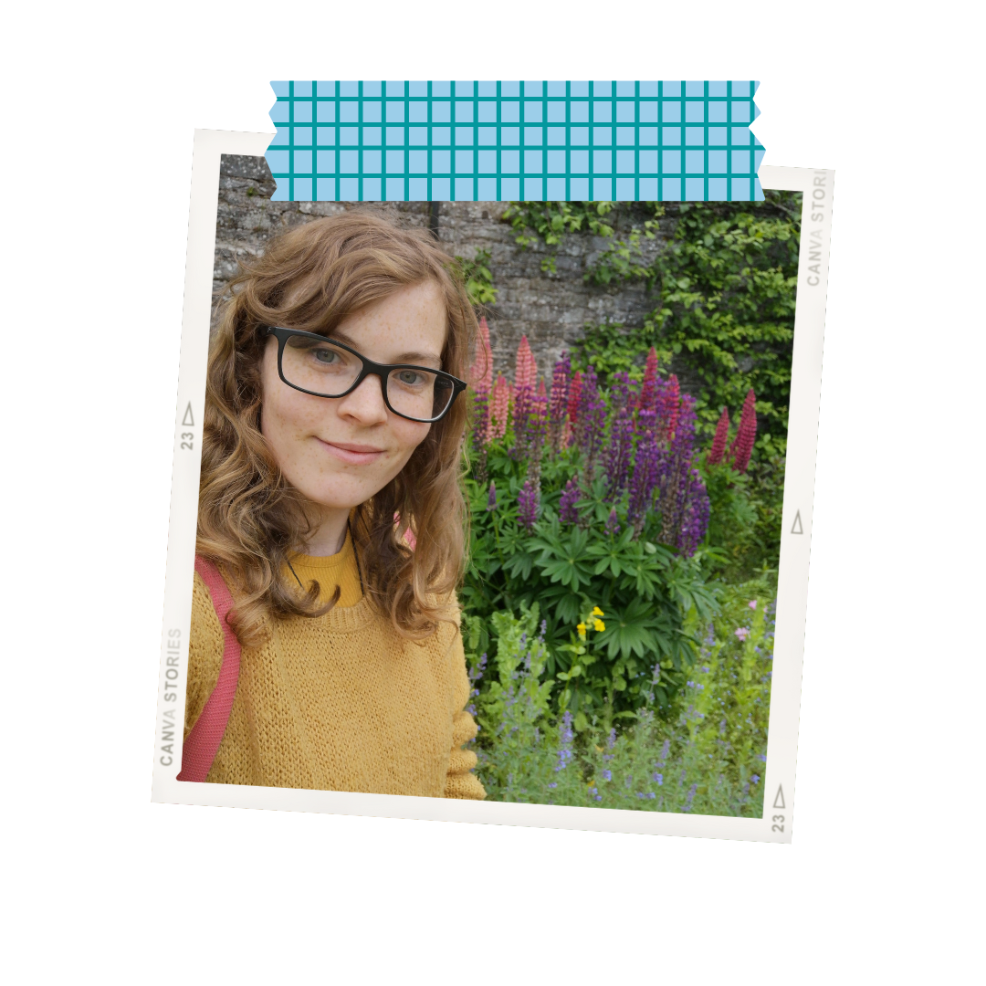 A polaroid-style photo of a white women with brown hair anc glasses wearing a yellow jumper in front of some lupin flowers. The photo is at a slight angle and is 'stuck down' with a graphic depicting washi tape.