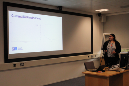 Image of the student delivering a presentation on her project. She is gesturing to graphs on a big screen