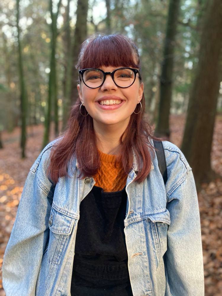 A photo of a young woman smiling, the background is in the woods