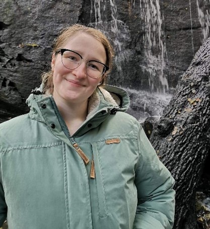 An image of Hannah, smiling standing in front of a waterfall