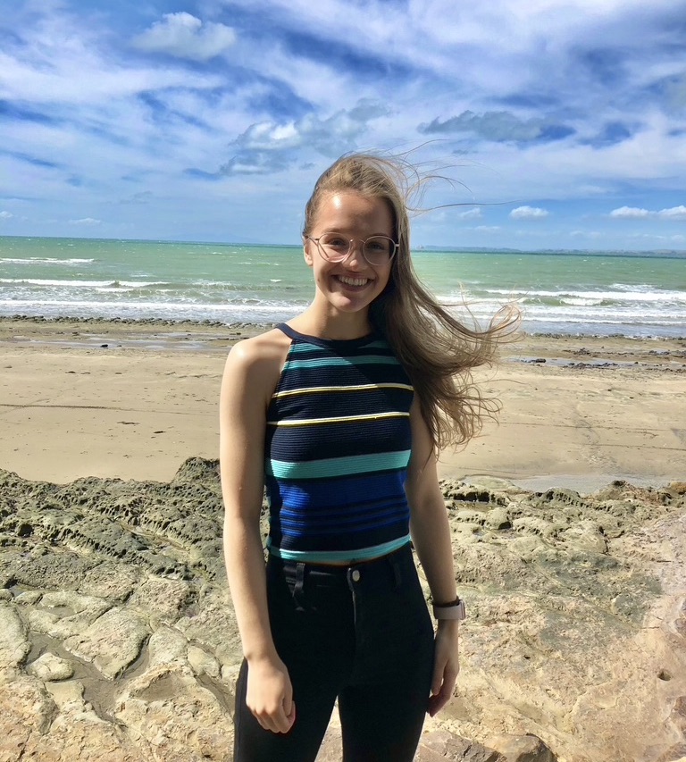 A girl on the beach, smiling at the camera.