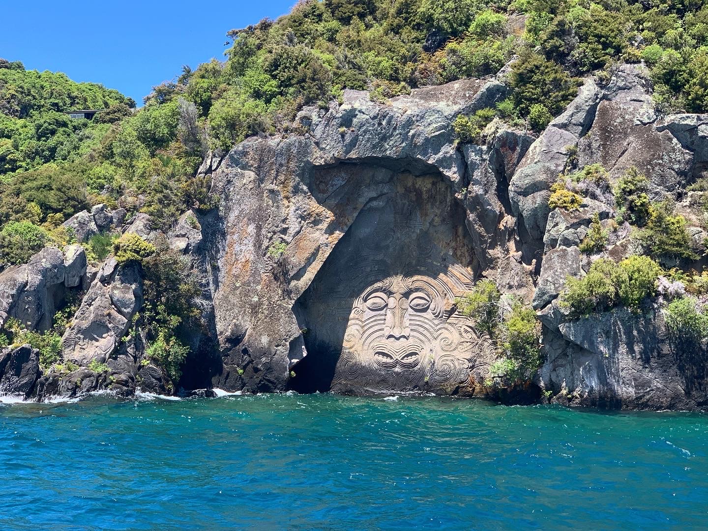 A rock face along the water's edge with a large carving of a face with two mouths.
