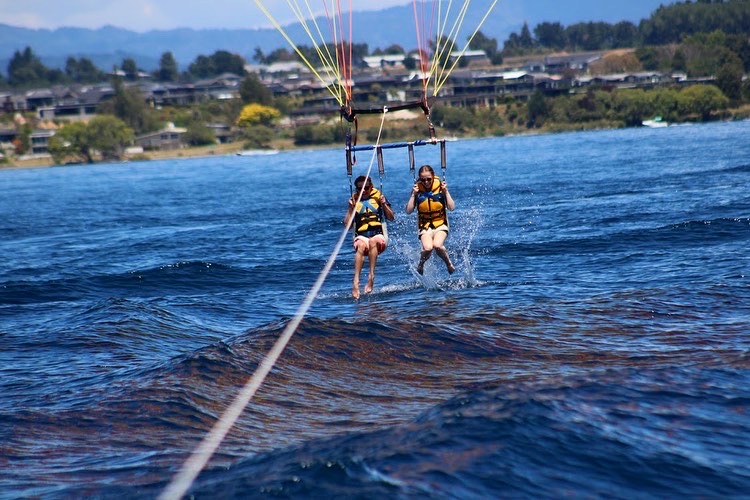 Two people parasailing, splashing their feet in the water.