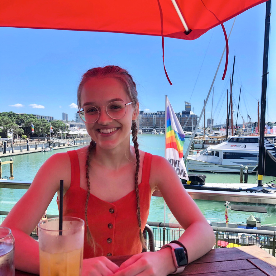 A girl smiling at the camera, with a harbour in the background.