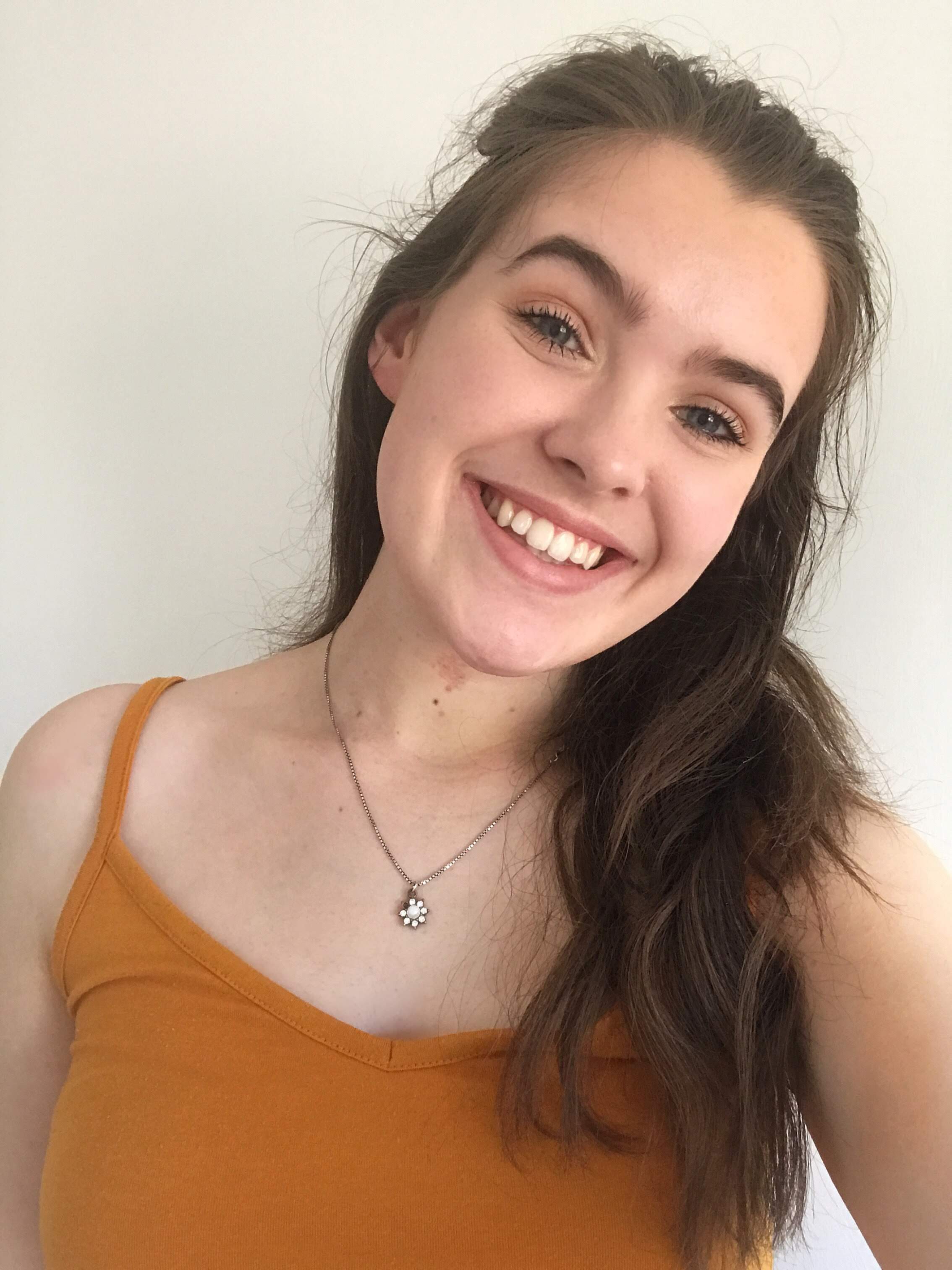 Image of the author - Cerys - smiling. She has long brown hair and is wearing an orange top.