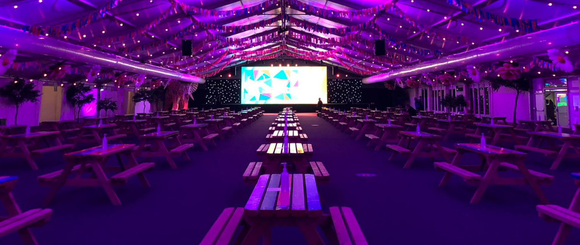 The Marquee a large COVID safe at The University of Surrey. It has a festival vibe with picnic tables, a large TV screen and a stage.