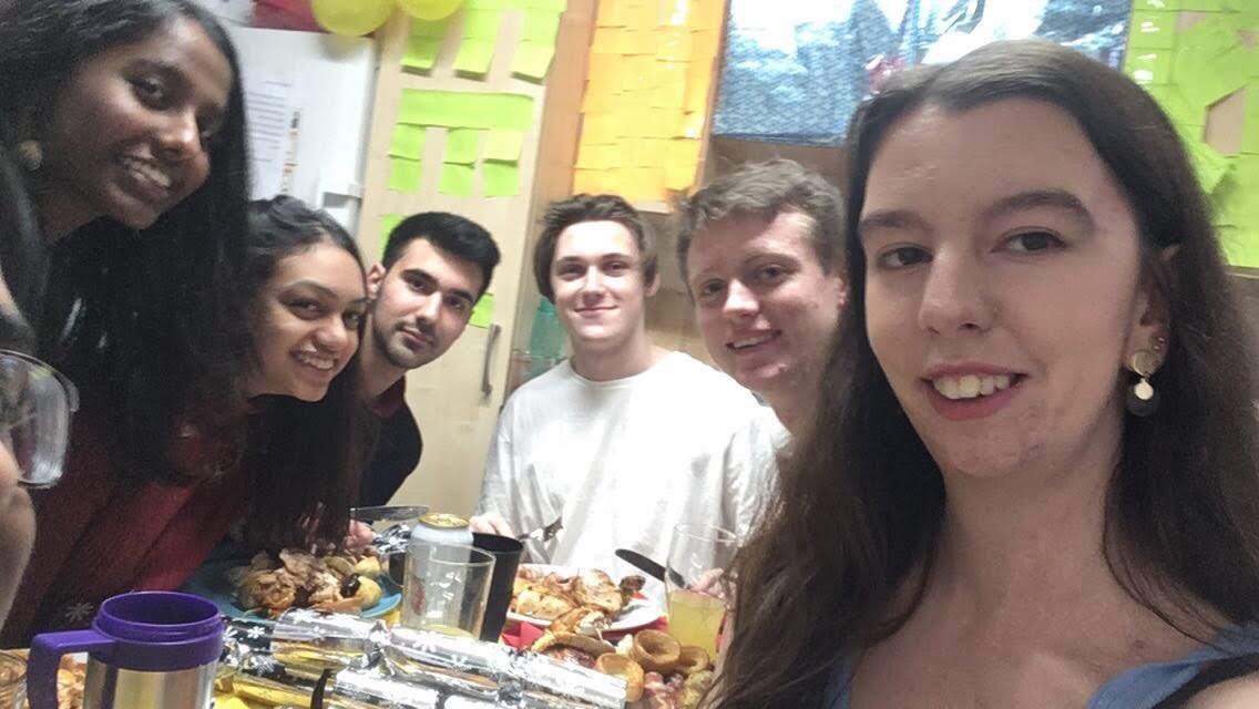 Group of friends smiling in shared kitchen eating a christmas dinner together they have cooked. 