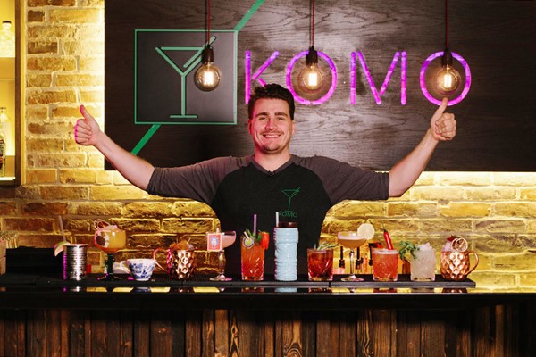 Komo Guildford bartender smiling with a row of cocktails in all different shapes, colours and cup types