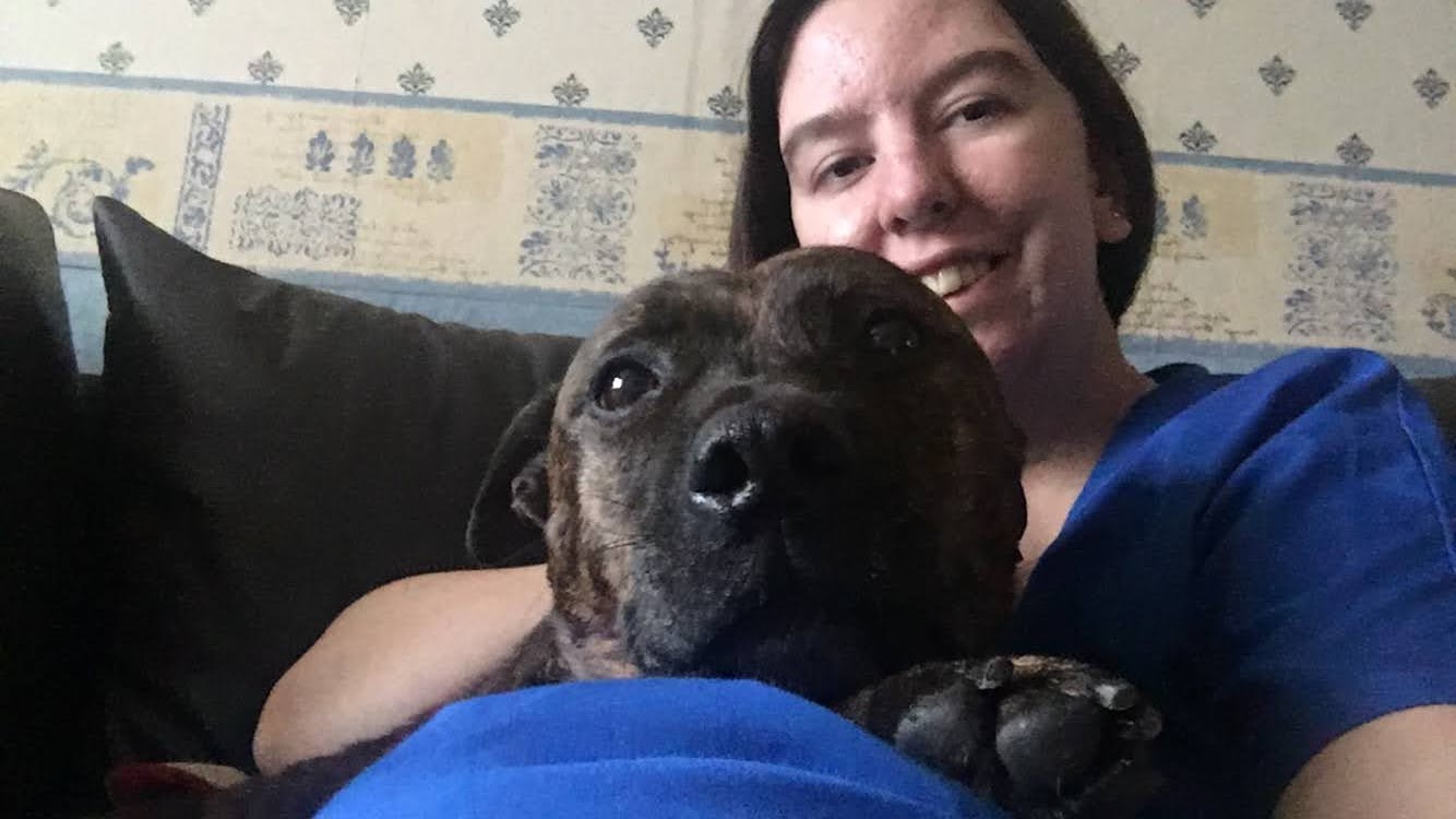 Uni of surrey vet student wearing blue scrubs cuddles a her own dog 