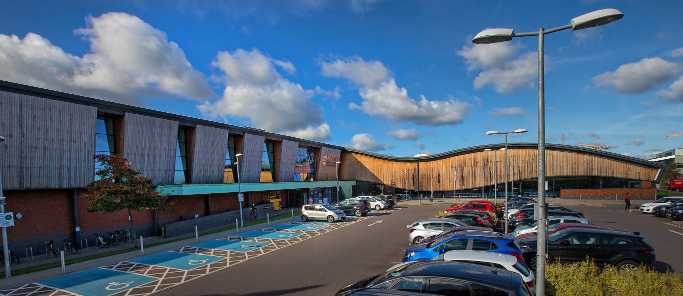 Wide shot of outside of Surrey Sports Park building with main entrance and car park