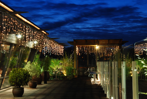 Thai Terrace palm deck outdoor dining area with fairy lights and small plants. Glass along border as roof top bar with view of Guildford 