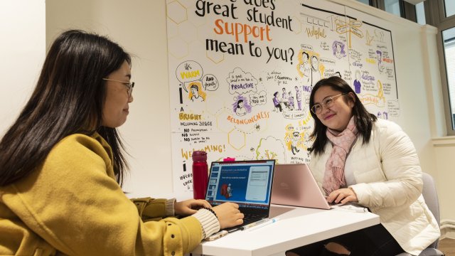 Student and academic smiling while discussing academic and learning support. Whiteboard in photo with ideas about, ' what does great student support mean to you?'.