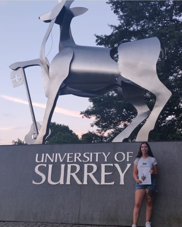 Surrey vet student in front of University of Surrey stag statue holding completed research paper 