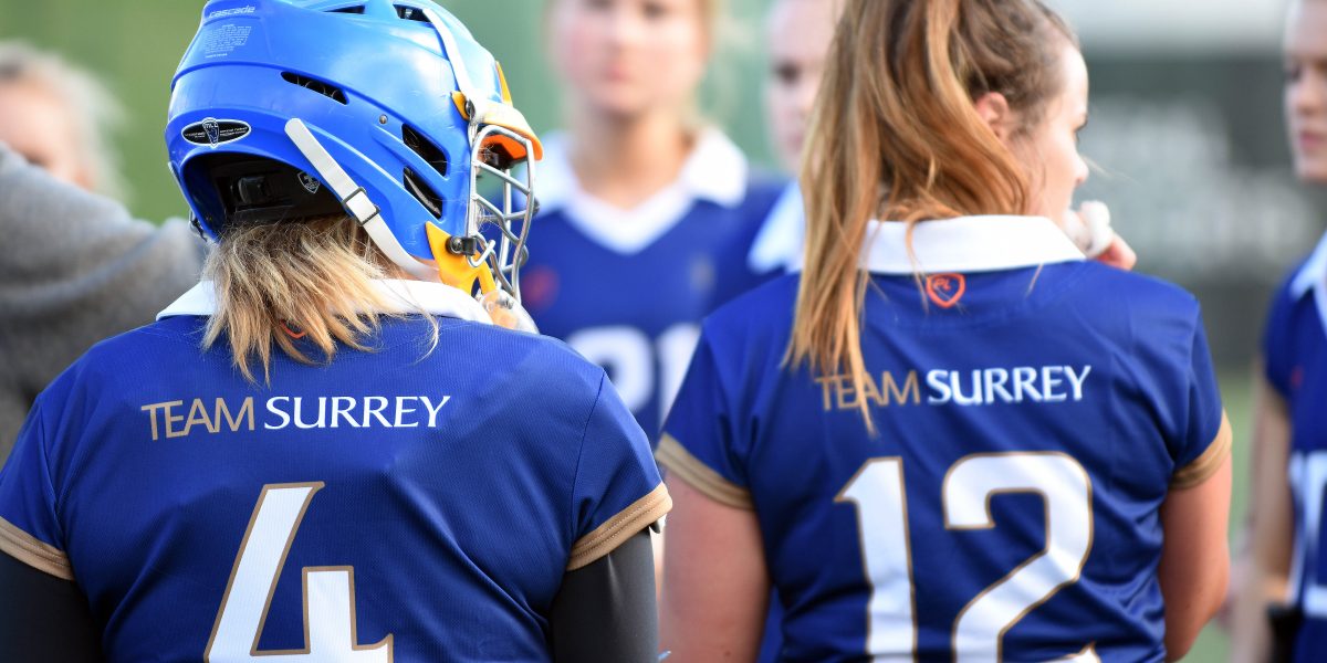 Womens Lacrosse team huddle wearing blue Team Surrey uniform and equipment.