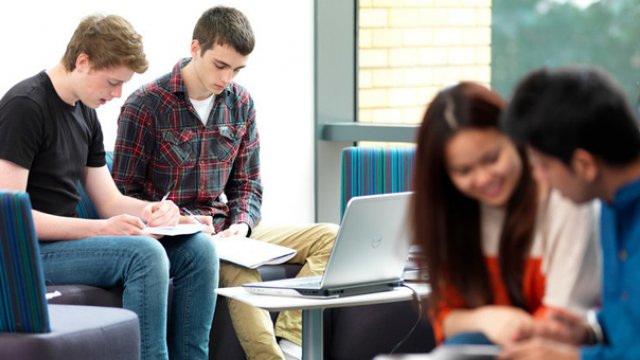 Students sat in pairs in library at The University of Surrey studying together on paper. 