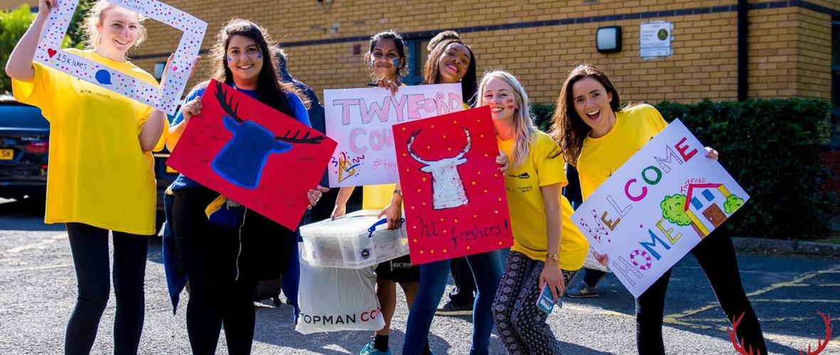 Group of students volunteering as Freshers Angels welcoming new students to university holding hand made signs. 