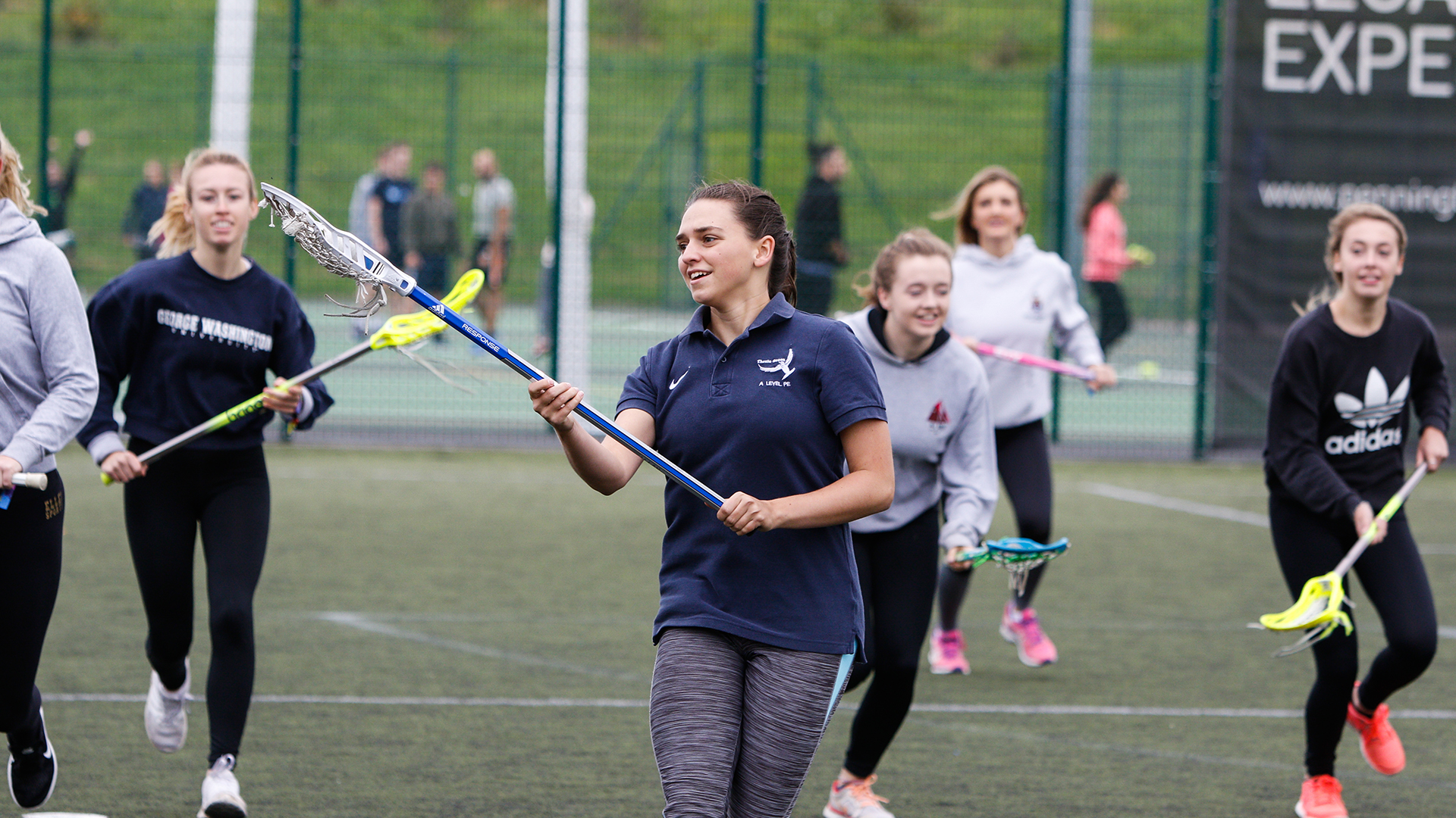 Group of female students running with Lacrosse sticks trying out Lacrosse sport